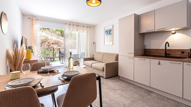 A modern kitchen with white cabinets, a wooden countertop, and a black faucet. There is a dining area with a wooden table and brown chairs. - L'Île de Beauté - Climatisé (Pietrosella)