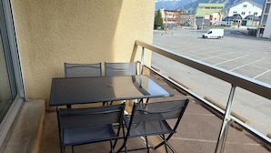 Un balcón con mesa y sillas, vista a un estacionamiento y edificios al fondo.