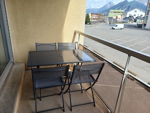 A balcony with a table and chairs, a view of a parking area, and buildings in the background. - Le Nid Pyrénéen - Proche station de ski (Saint Lary-Soulan)