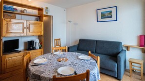 Una sala de estar acogedora con una mesa redonda de comedor preparada para cuatro personas, un sofá azul y un mueble de madera con televisor y cafetera.