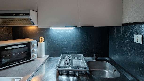 Una cocina con horno tostador empotrado, escurreplatos, lavamanos e iluminación en la pared.