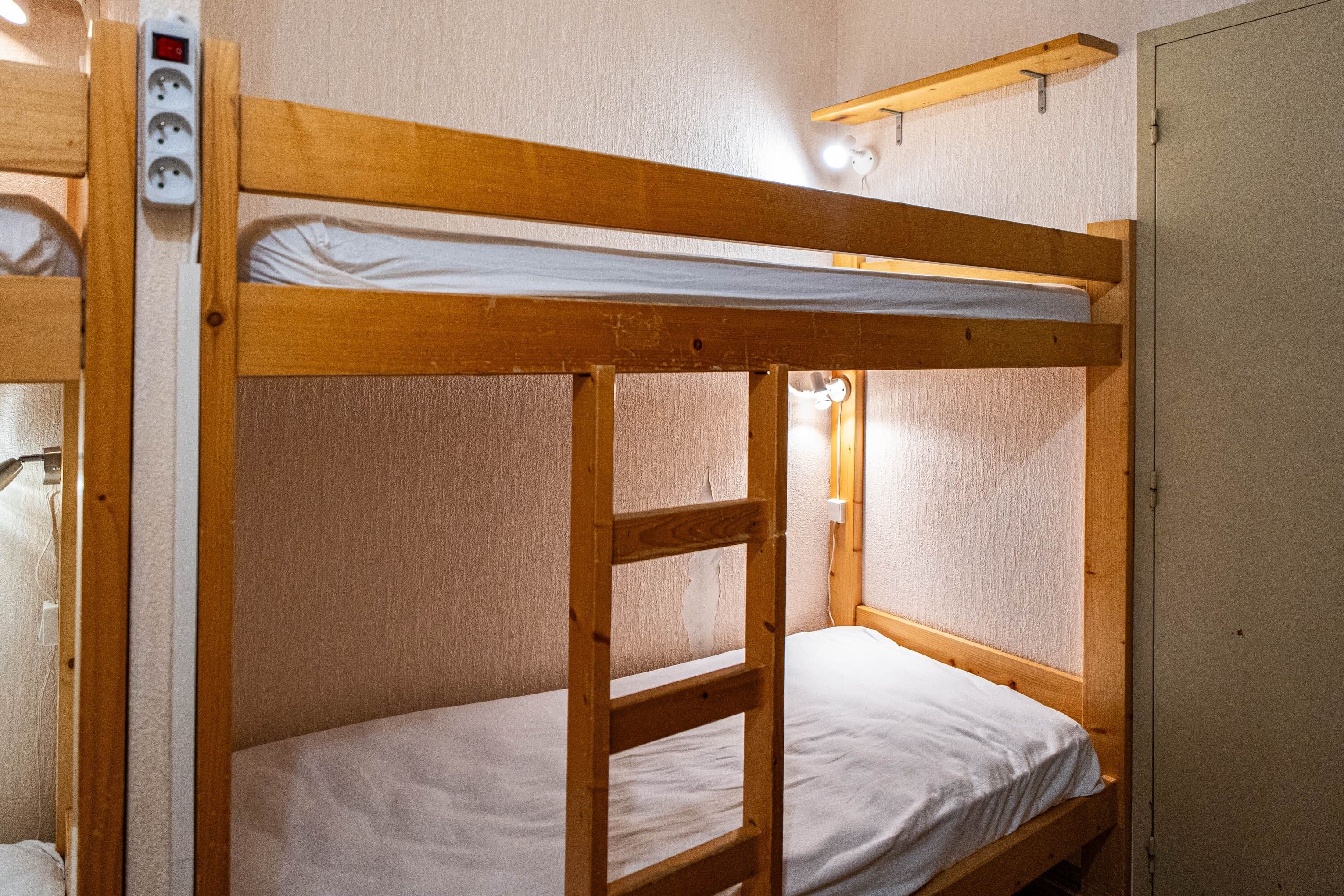 Ein Stockbett mit Holzrahmen, einer weißen Matratze und einer an der Wand befestigten Steckdose.