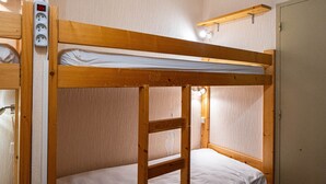 Una cama litera con estructura de madera, colchón blanco y un enchufe eléctrico en la pared.