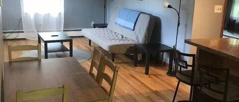 Un'ampia zona giorno con un tavolo da pranzo in legno, sedie, un divano e un tavolino. C'è una lampada e un quadro appeso al muro.