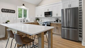 A modern kitchen with white cabinetry, stainless steel appliances, and a large island with two chairs.