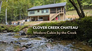 A modern cabin by a creek with a deck and outdoor seating.