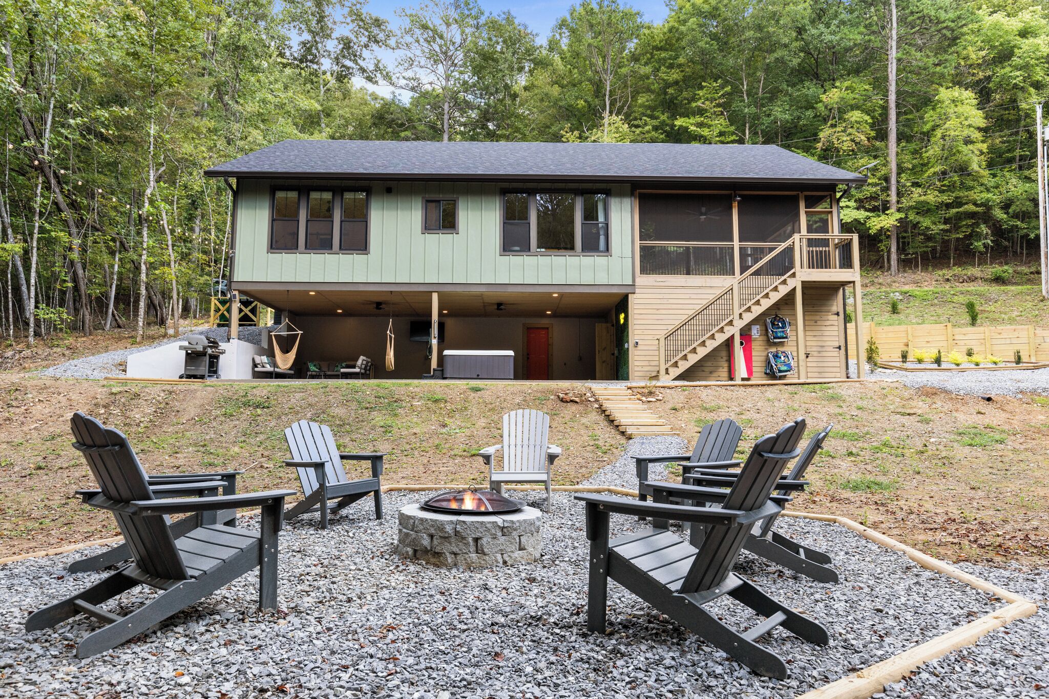 A two-story cabin with a deck and a fire pit area with Adirondack chairs.