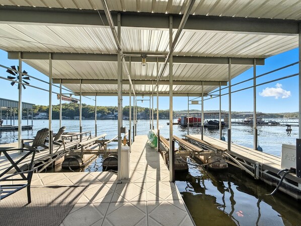 A covered dock area with chairs and tables, a view of the water, and boats in the background.