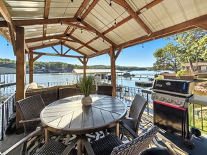 A covered outdoor seating area with a round table and wicker chairs, overlooking a body of water with boats and a dock in the background.