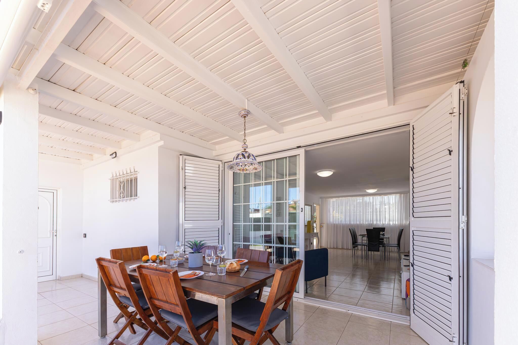 A dining area with a wooden table and chairs, a chandelier, and a sliding glass door leading to another room.