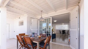 A dining area with a wooden table and chairs, a chandelier, and a sliding glass door leading to another room. - Careva Suites 21 by VillaGranCanaria (San Bartolomé de Tirajana)