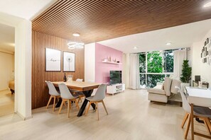 A modern living room with a wooden ceiling, a dining area with a wooden table and chairs, a pink accent wall, and large windows with a view of greenery. - Acogedor apartamento tipo boutique cerca d Reforma (Mexico City)