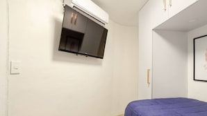 Una camera da letto con un letto, una TV a parete e un armadio bianco.