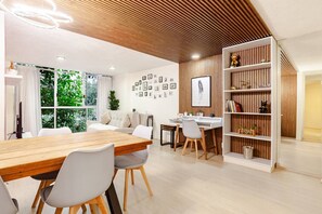 Een moderne woonkamer met een houten plafond, een eethoek met een houten tafel en stoelen, een witte bank en een boekenkast.