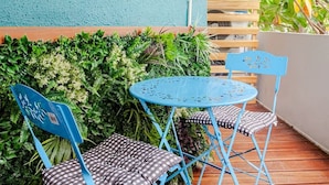 Un patio con tavolo e sedie in metallo blu, circondato da piante rigogliose e un recinto in legno.