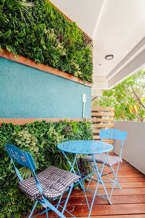Eine Terrasse mit blauem Metalltisch und -stühlen, umgeben von üppigem Grün und einem Holzzaun.