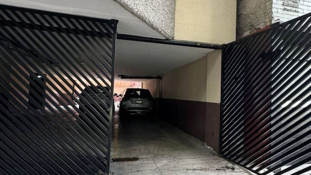 Un parcheggio sotterraneo con un'auto al suo interno, una scala che conduce a un piano superiore e un ingresso con cancello.