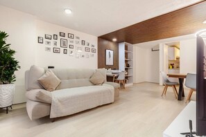 A modern living room with a sofa, a dining area, and a kitchen visible through an open doorway.