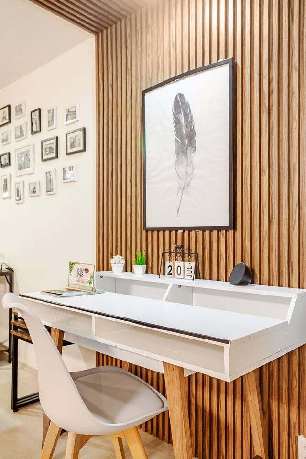 Ein moderner Arbeitsbereich mit weißem Schreibtisch, einem gerahmten Federkunstwerk und einer Wand aus Holzlatten.
