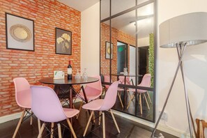 Uma sala de conferência moderna com parede de tijolos, cadeiras cor-de-rosa, uma mesa redonda e um espelho grande que reflete o ambiente.