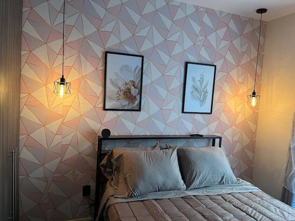 A bedroom with a geometric-patterned wall, a bed with a headboard, and two wall-mounted light fixtures.
