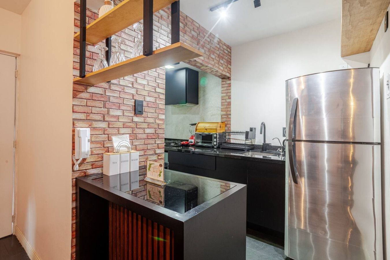 A modern kitchen with a brick wall, a stainless steel refrigerator, and a coffee machine.
