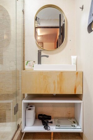 A bathroom with a wooden vanity, a round mirror, a sink, and a shelf with toiletries.