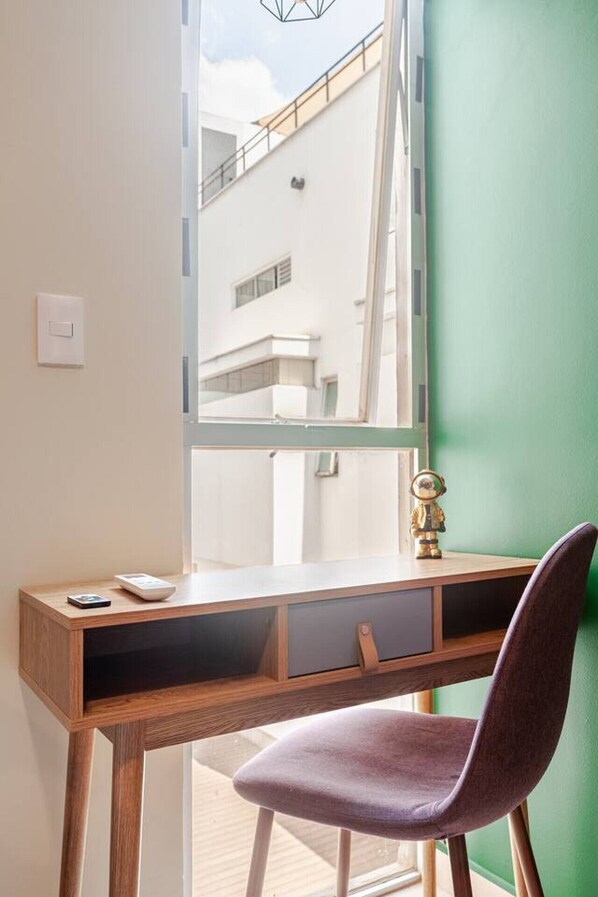 A study area with a wooden desk, a purple chair, a small globe, and a window overlooking a building.