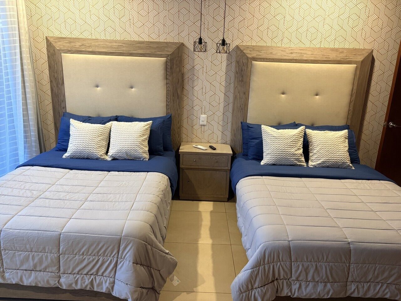 A double room with two beds, each with a headboard, a nightstand, and a patterned wallpaper.