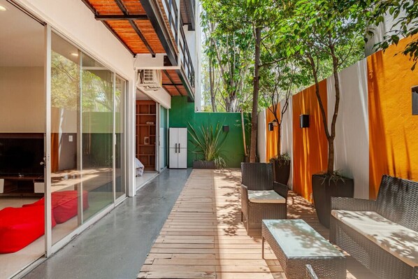 A modern outdoor patio with a glass door leading to a living area, a wooden deck, and outdoor furniture.