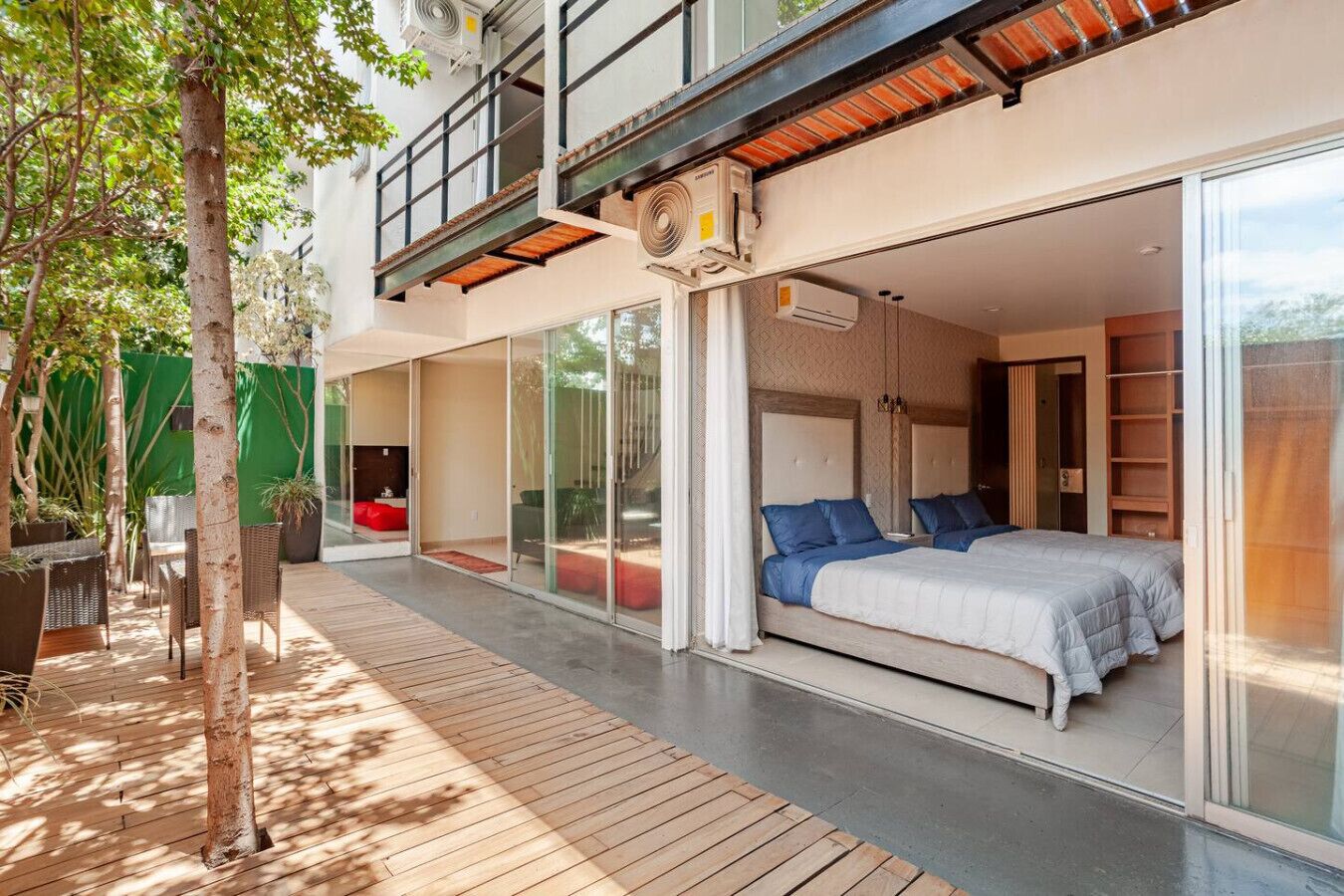 A modern bedroom with a large bed, sliding glass doors, and a balcony with outdoor seating.