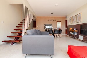 A modern living room with a grey sofa, wooden staircase, dining area, kitchen, and a TV on the right. - Duplex 3BR con terraza y parking I Roma Sur (Mexico City)