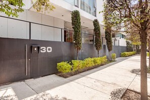 A modern building with a grey facade, numbered 30, featuring a clean, straight-lined design with a small entrance and a pathway lined with trimmed bushes and trees.