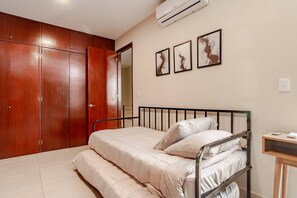 A bedroom with a bed, wooden wardrobe, and three framed artworks on the wall.