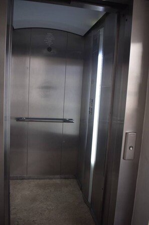 A metallic elevator interior with a handrail and a control panel.