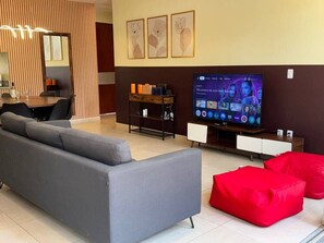 A modern living room with a grey sofa, red bean bag chairs, a TV, and a wooden sideboard.