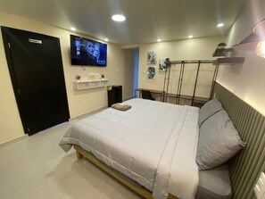 Une chambre avec un lit, un téléviseur fixé au mur, une étagère avec divers objets et une porte sur laquelle est inscrit « M. Pumper ».