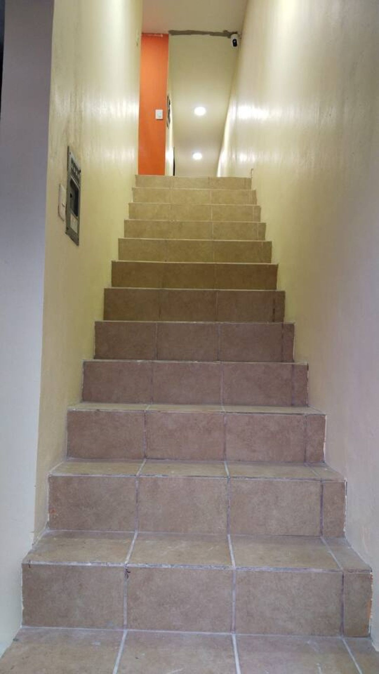 Una escalera con baldosas color beige que lleva a una puerta naranja al final.