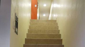 Una escalera con baldosas color beige que lleva a una puerta naranja al final.