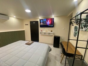 Une chambre d’hôtel avec un lit, un téléviseur fixé au mur, une petite table et une étagère ornée d’objets décoratifs.