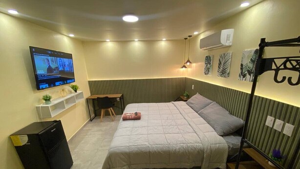 Et kompakt hotelværelse med seng, skrivebord, stol, fjernsyn og en lille hylde med pynteting.