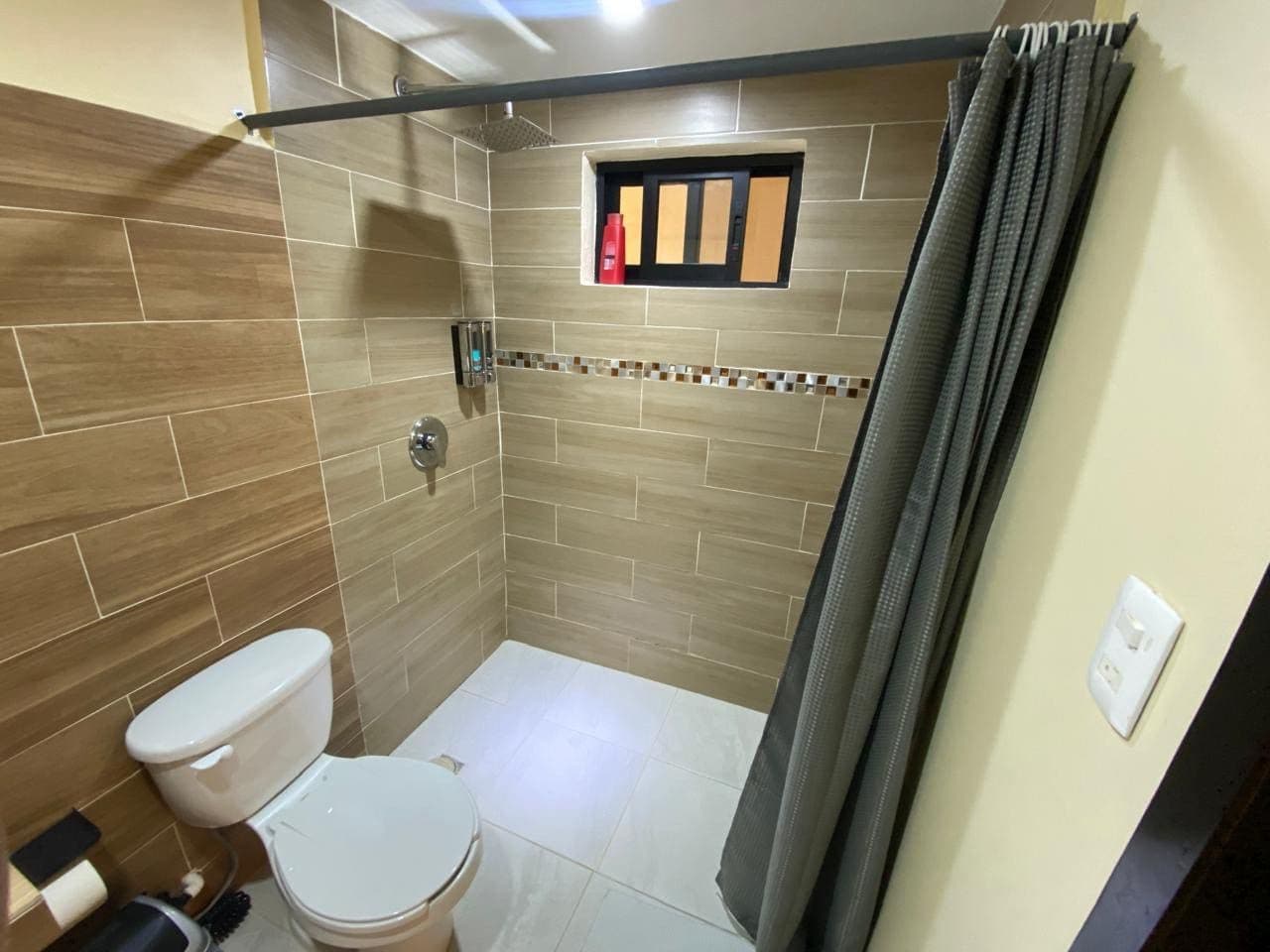 A bathroom with a shower, toilet, and a small window.