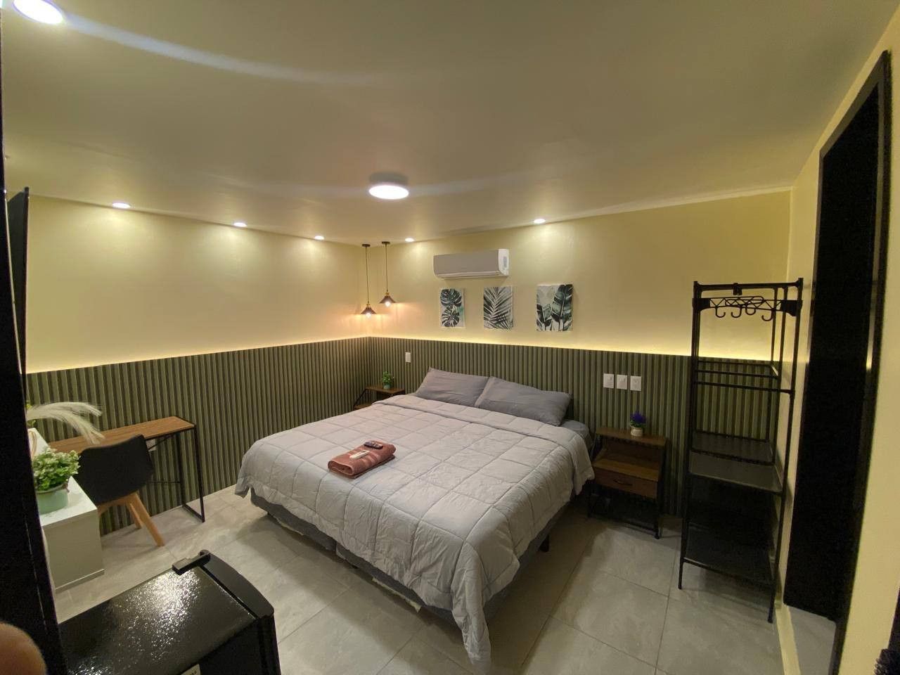 A bedroom with a bed, bedside tables, a desk, an air conditioning unit, and a hanging chair.