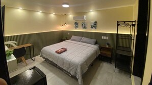 Un dormitorio con cama, mesitas de noche, escritorio, aire acondicionado y una silla colgante.