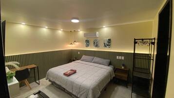 A bedroom with a bed, bedside tables, a desk, an air conditioning unit, and a hanging chair.