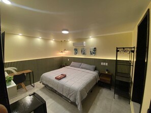 Een slaapkamer met een bed, nachtkastjes, een bureau, een airconditioning en een hangstoel.