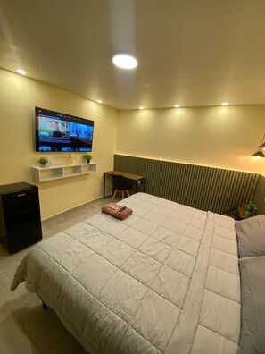 Hotelkamer met een groot bed, een flatscreen televisie aan de muur, een klein bureau en een radiator.