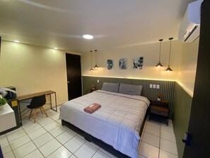 A hotel room with a bed, a desk, and a chair. There are wall-mounted lights and a small table with a plant. - Mini Hotel Chetumal - Room 3 - King Bed (Chetumal)
