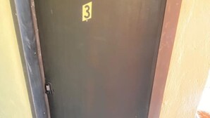 Uma porta escura com uma pequena placa indicando o número 3, um puxador e um chão de azulejos.