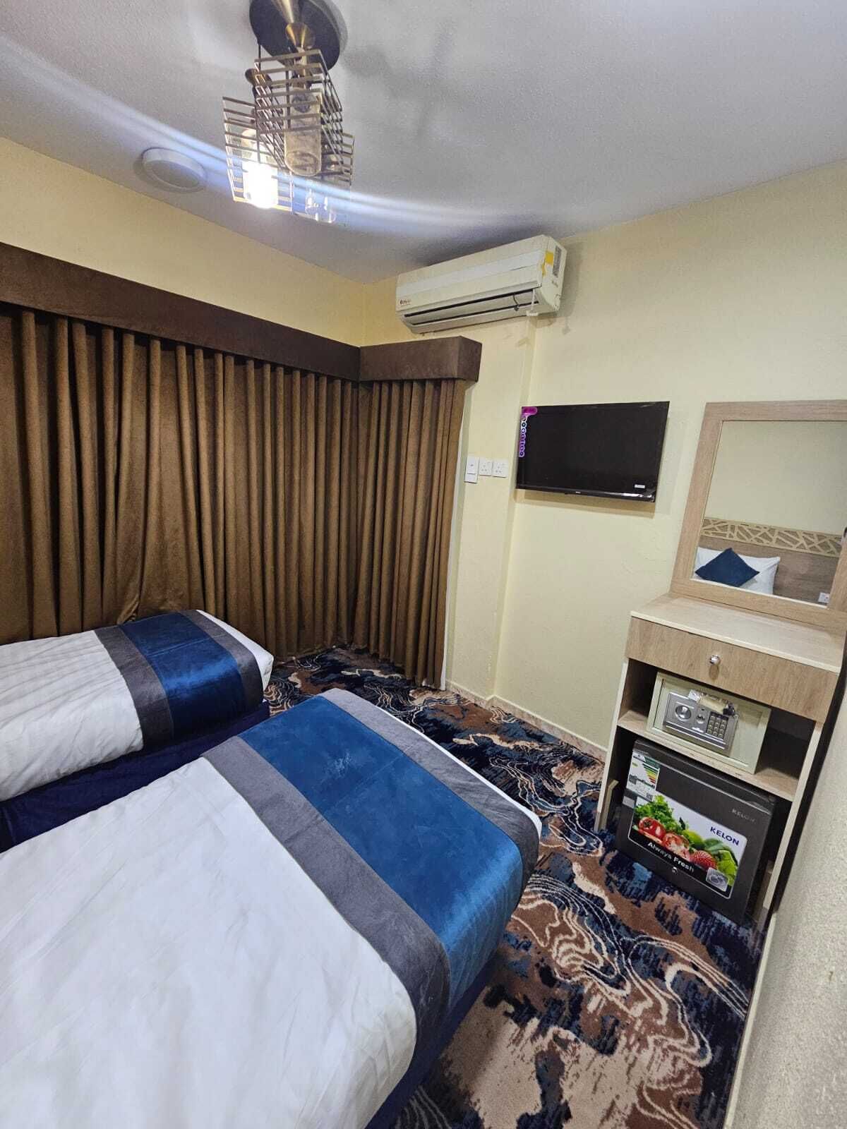 A hotel room with two beds, a flat-screen TV, an air conditioning unit, and a small wooden cabinet with a radio.